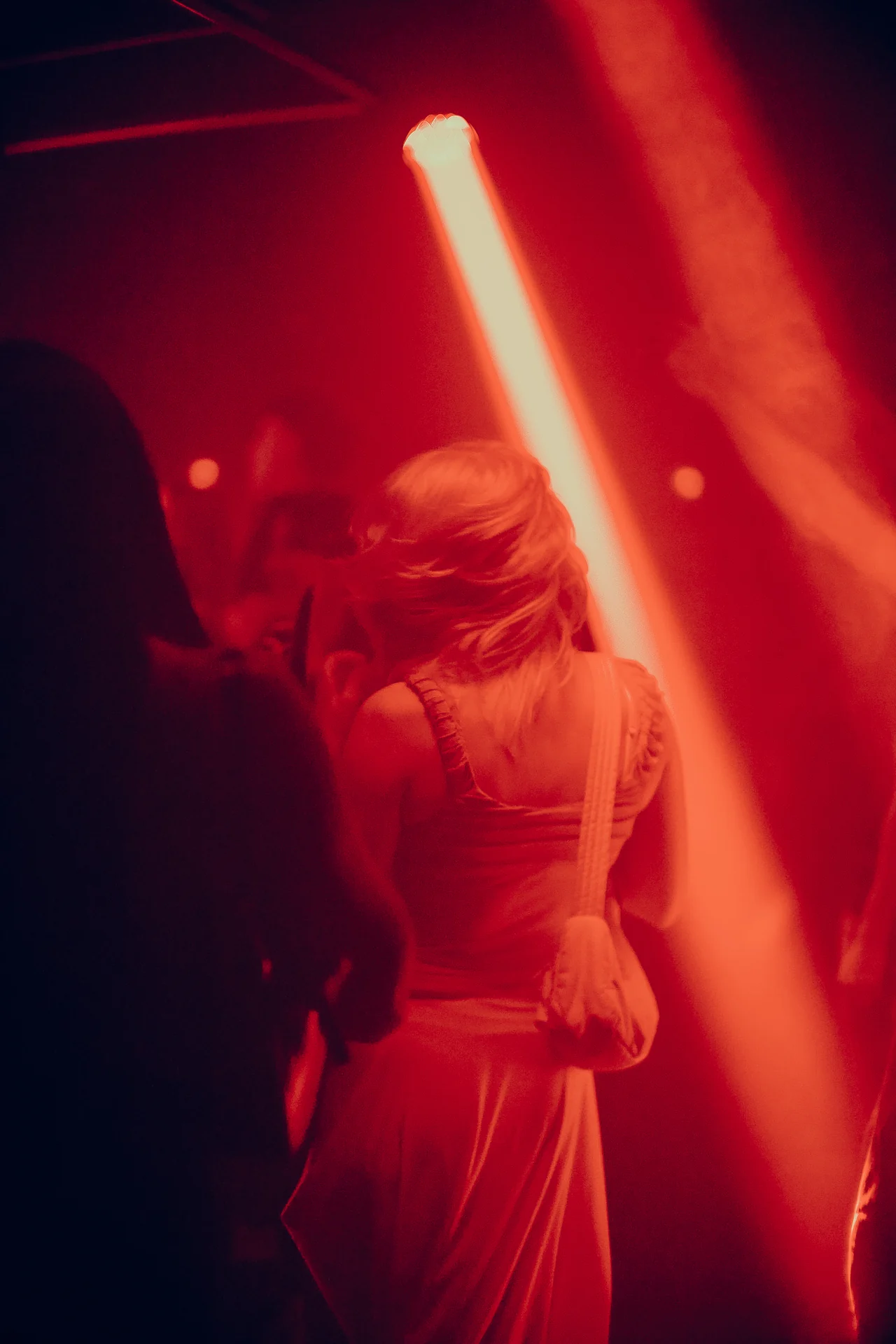 A dancer in sunglasses turns beneath a diagonal red spotlight.