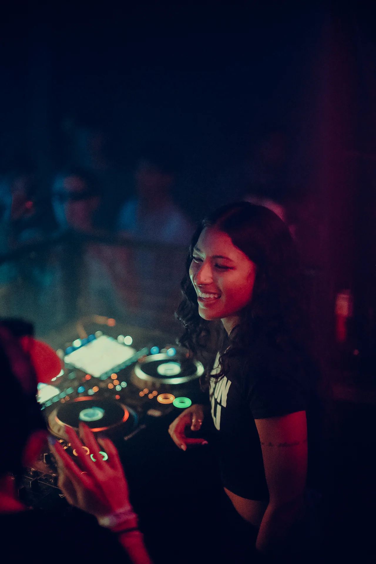 A smiling DJ looks across the decks in blue-green and magenta light.