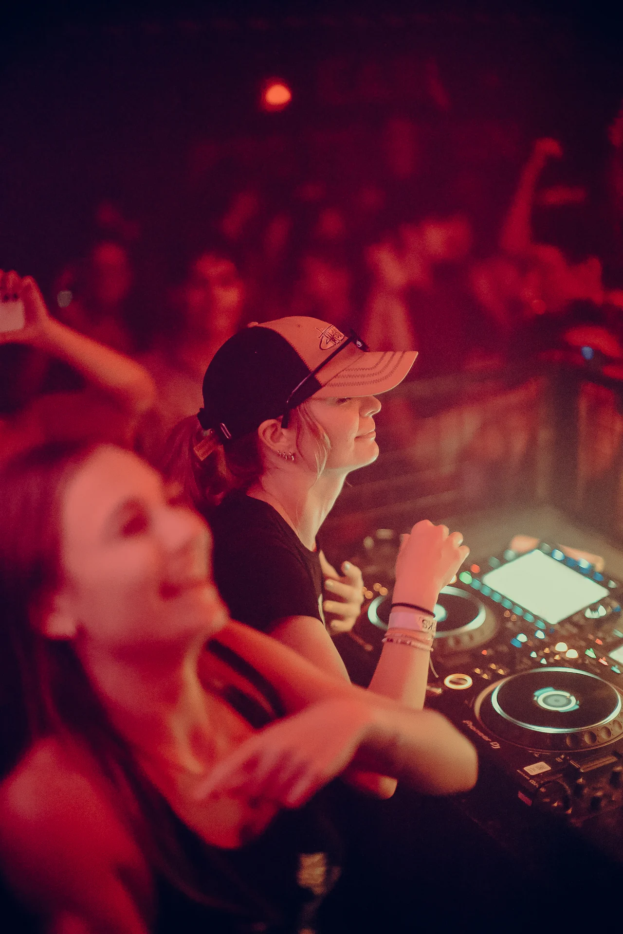 Two DJs share the booth, with a capped performer smiling above the mixer.