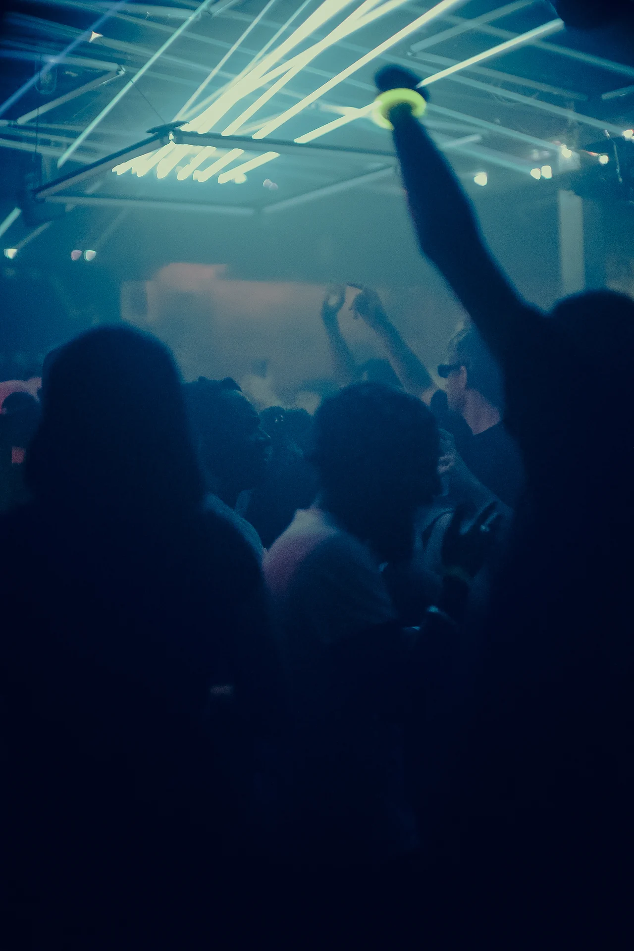 A raised arm breaks the silhouette of the crowd beneath bright crossing laser beams.