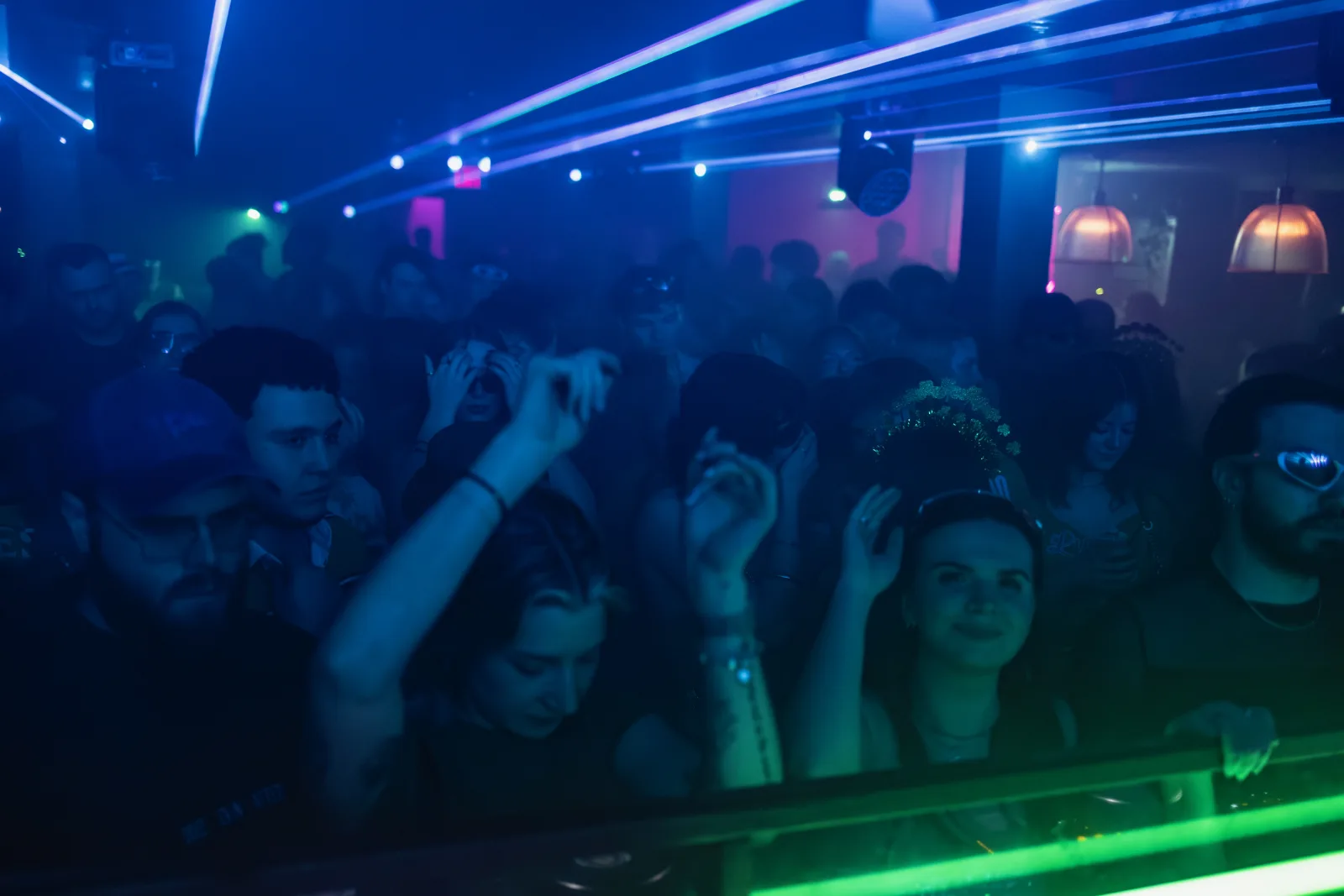 A packed dance floor beneath blue and green beams.